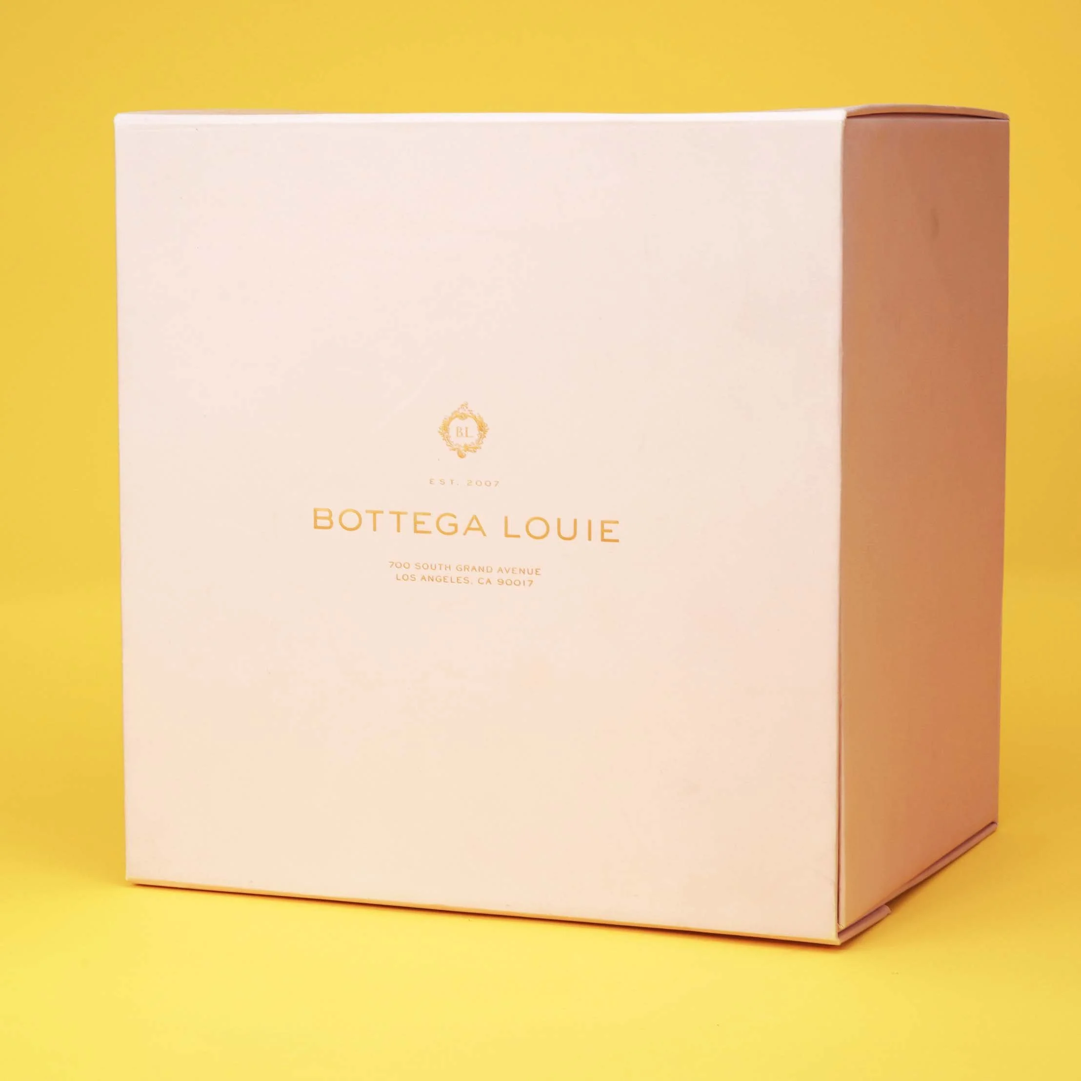 A white box with gold text and logo on a yellow background, labeled 'Bottega Louie' with an address in Los Angeles, CA.