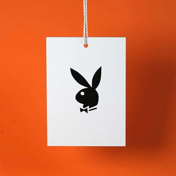 A white tag with a hole at the top, hanging by a striped string, featuring the black Playboy Bunny logo with a bow tie, against an orange background.