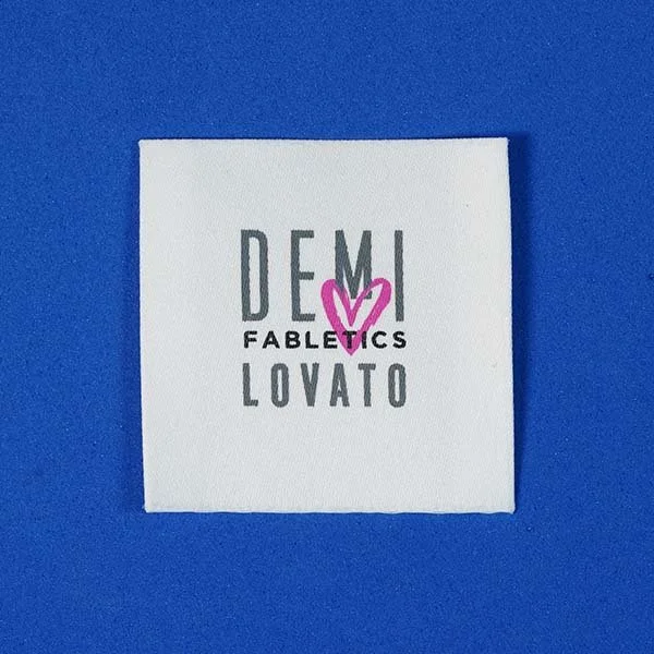 A square white card with the words 'Demi Lovato' and 'Fabletics' printed on it, and a pink heart with a smaller heart inside it.