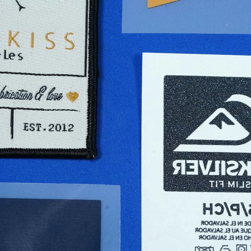 Close-up of two logos on a blue background, one embroidered patch and one printed sticker, partially visible.