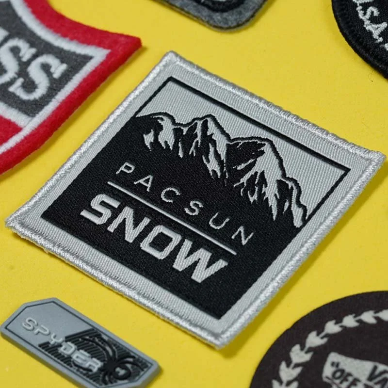 A close-up of a fabric patch with a mountain design and the words "PASCUN SNOW," placed on a yellow surface along with other patches.