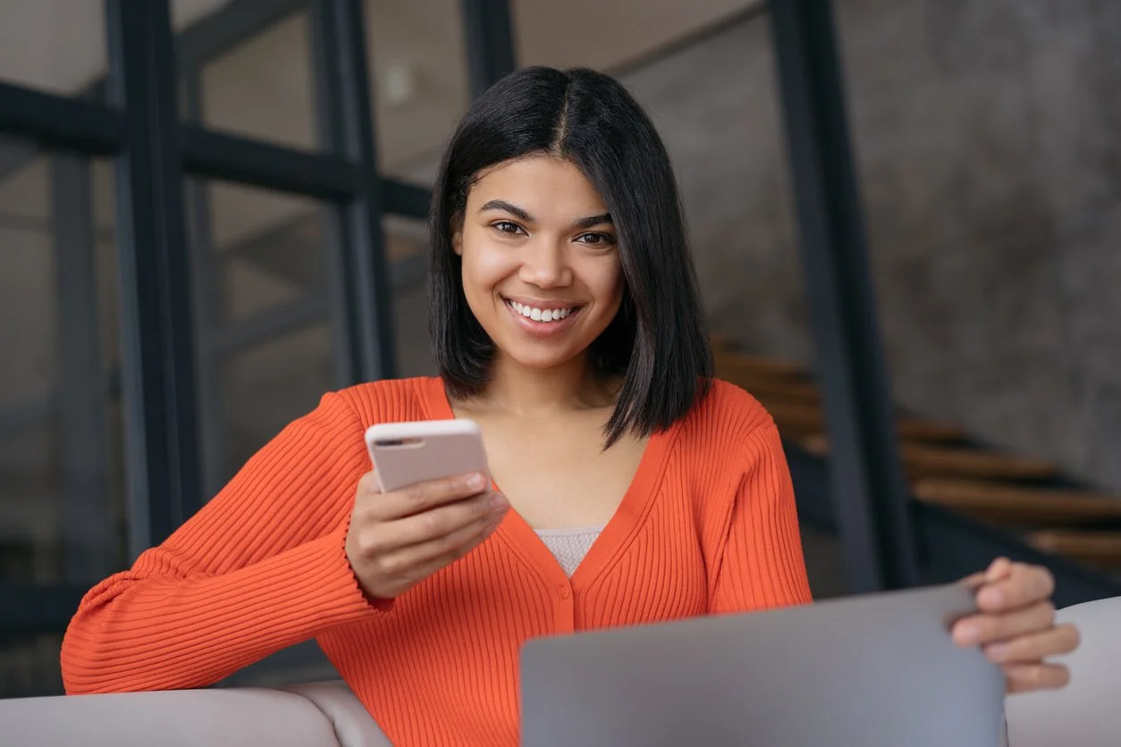 Young woman with black hair smiling while looking at her smartphone.