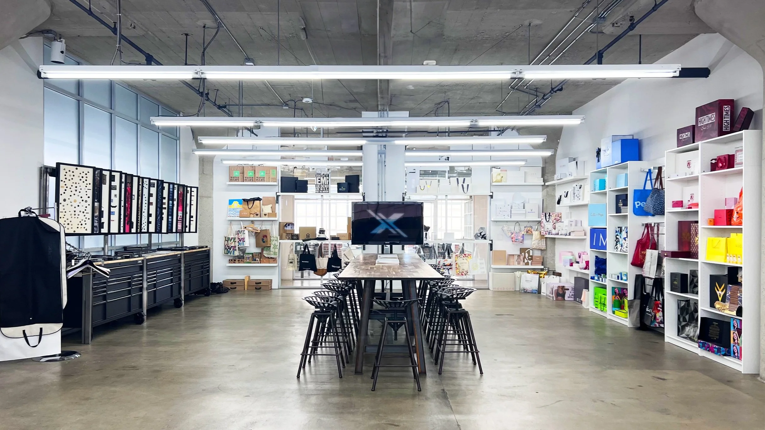 Interior of a retail store with shelves and display cases, a central table with chairs, and bright lighting.