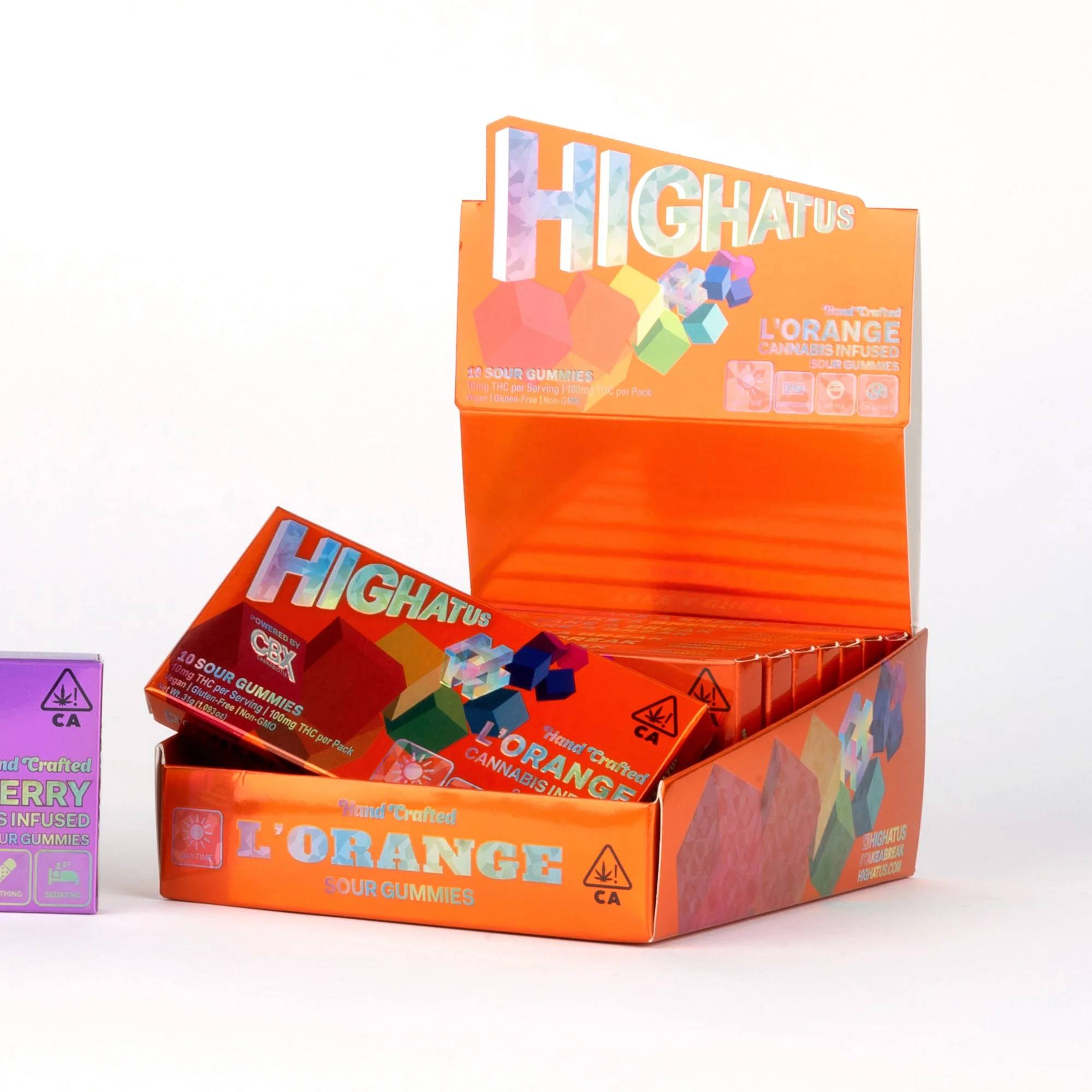 Open orange box of Higheratus L'Orange sour cannabis-infused gummies with one pack partially outside the box, and a purple box of similar gummies partially visible on the left.