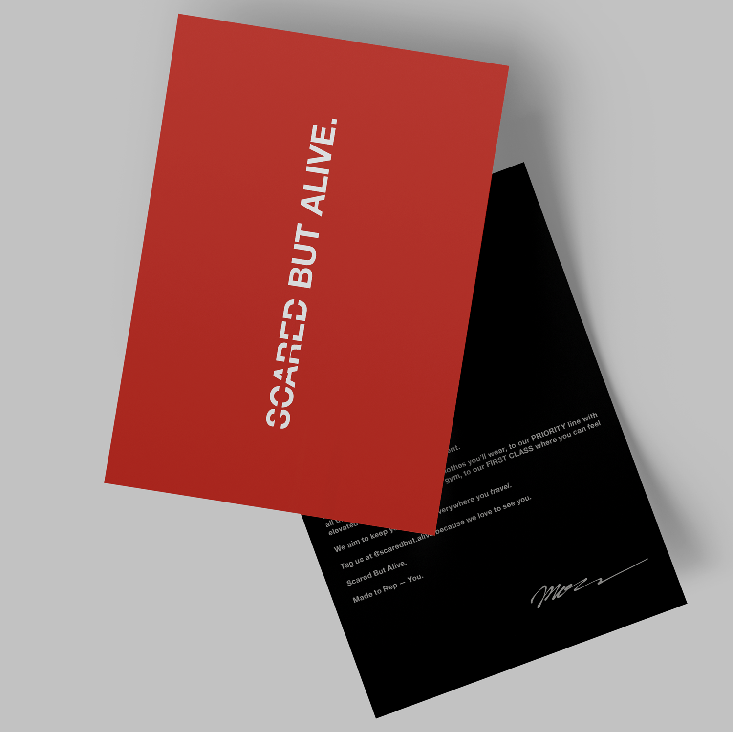 Two business cards, one red with white text saying 'SCARRED BUT ALIVE:' and one black with white text, lying on a light-colored surface.