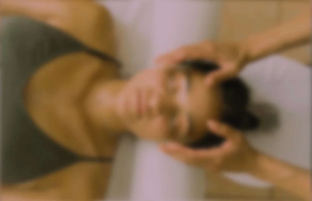 A woman taking a selfie with her phone, wearing a black tank top and leaning against a wall.