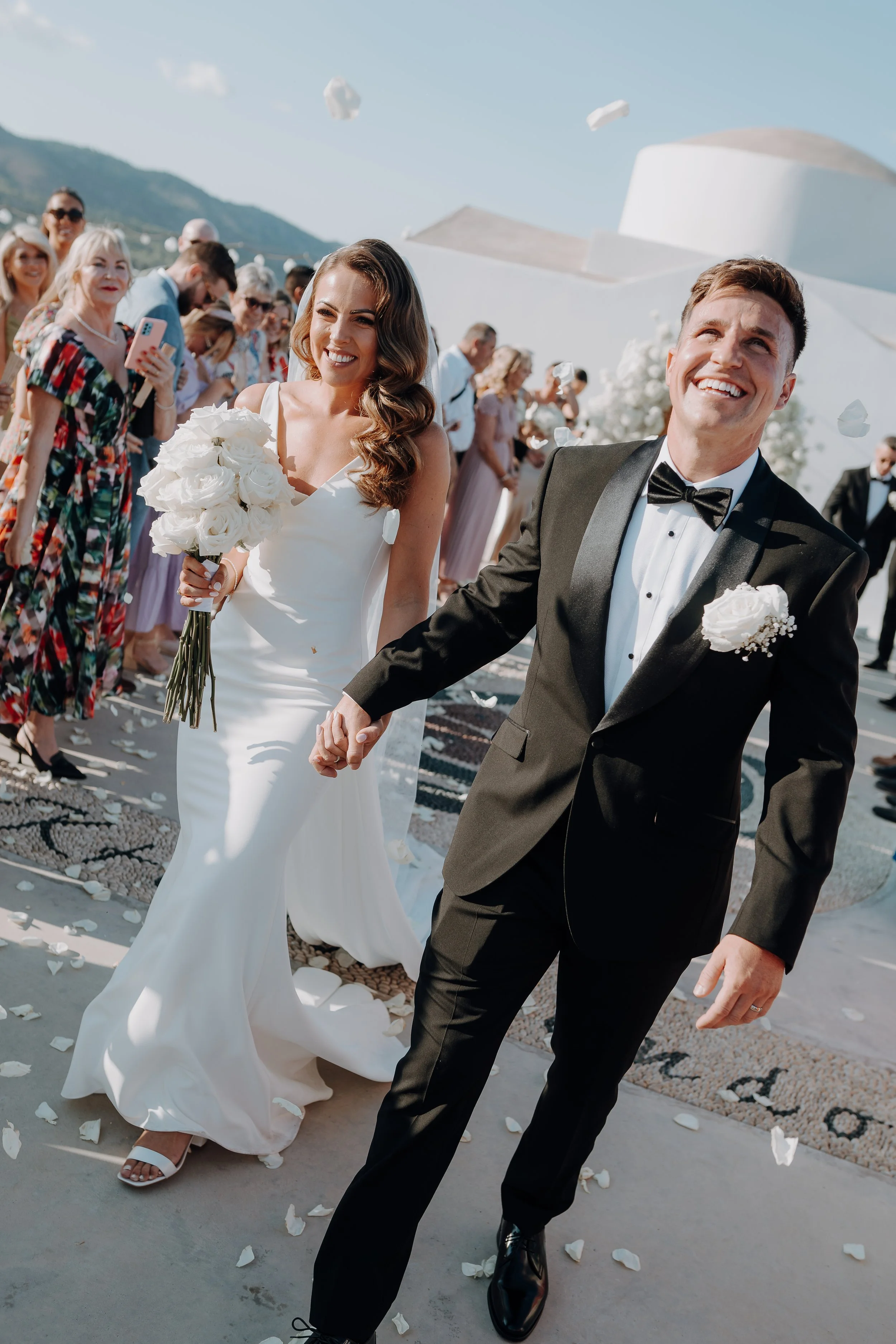 Four women celebrating outdoors during sunset, taking a selfie, smiling, holding a wine glass, and embracing each other.