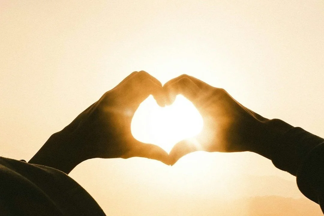 Hands forming a heart shape with the sun shining through the center.