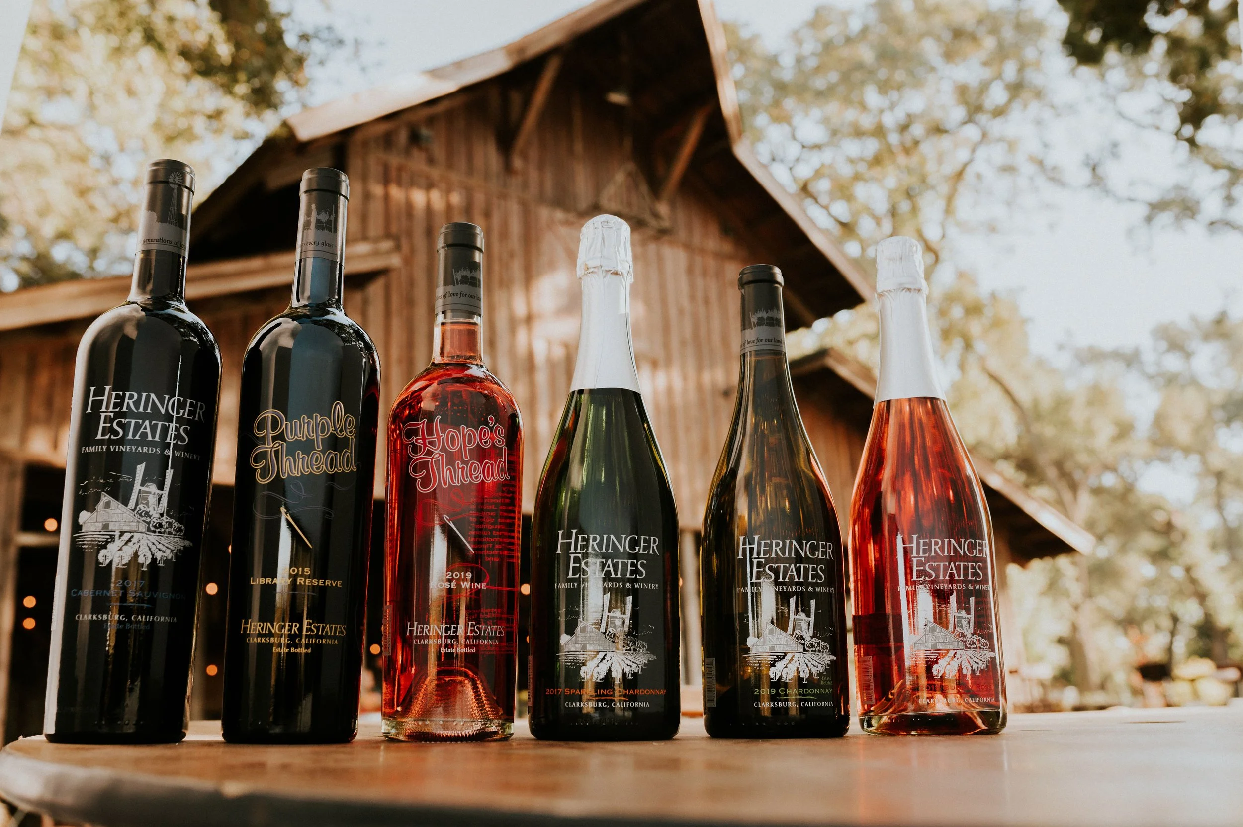 Six bottles of wine from Heringer Estates Winery in front of a wooden barn, with trees in the background.
