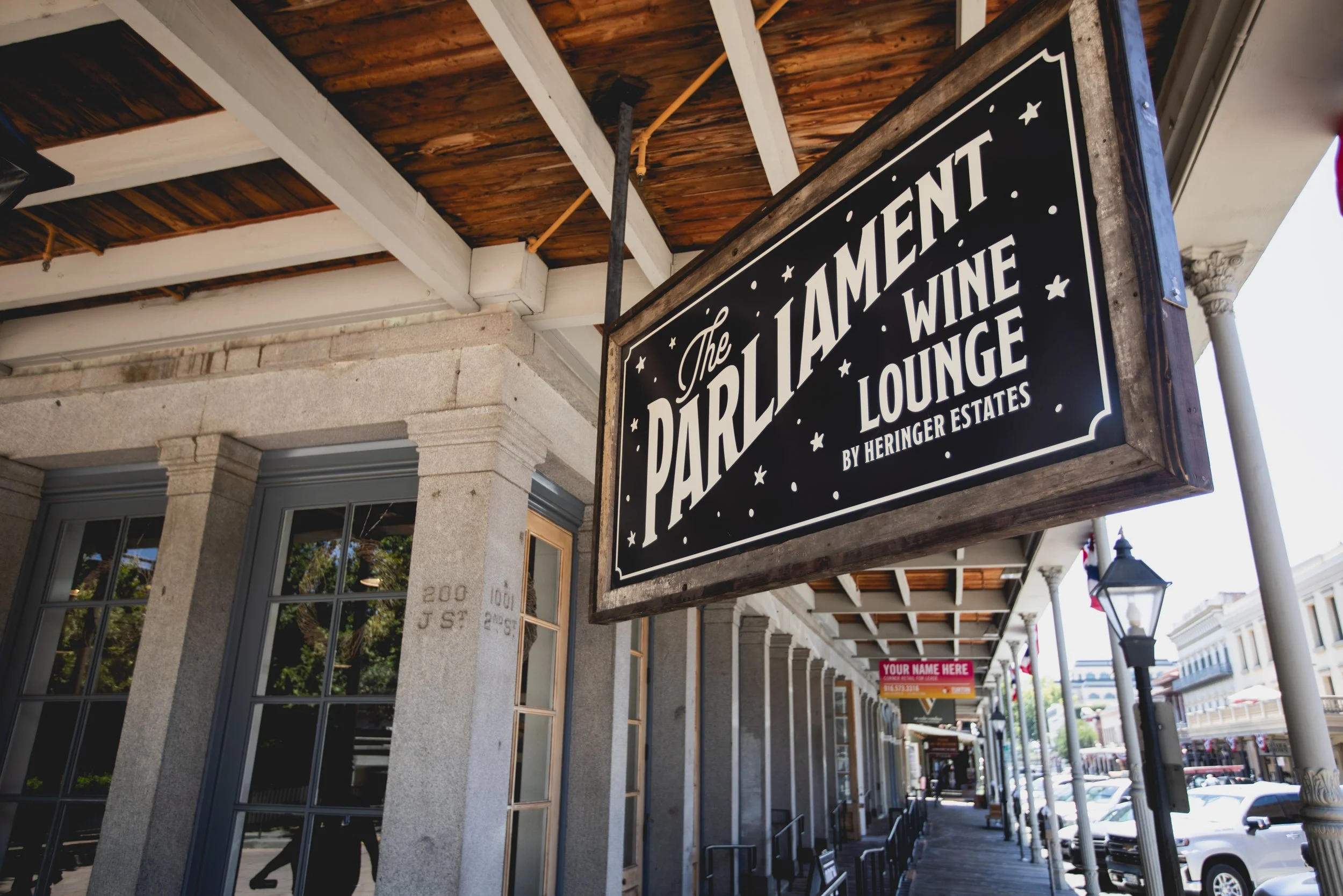 Sign for The Parlorliament Wine Lounge by Heringer Estates hanging outside a building in a retail area.
