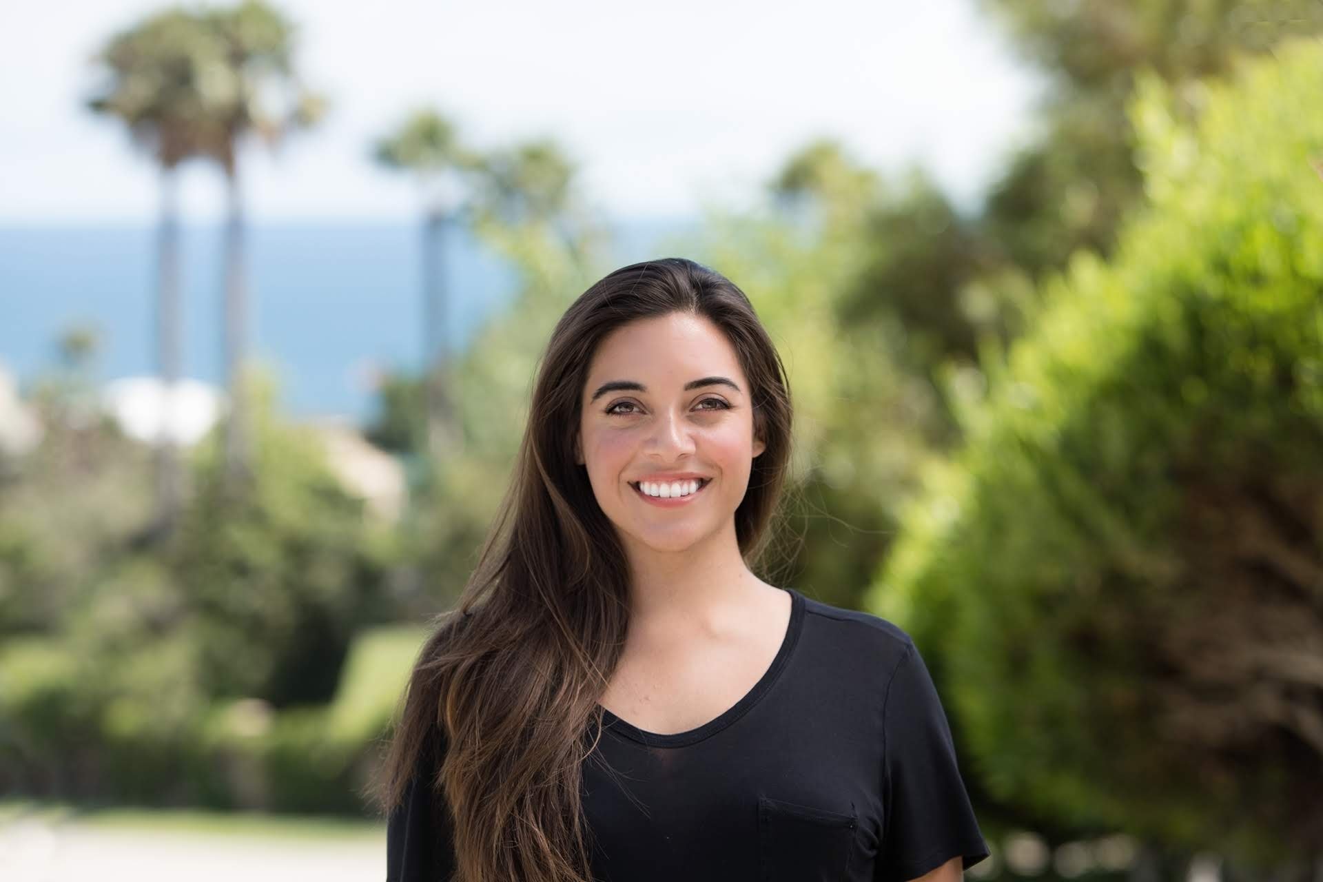Dr. Sylvia Martin wearing a black top outdoors with green trees and a blue sky in the background.
