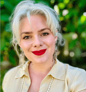 Elyse Jung-Vrymoed, AMFT, wearing red lipstick in front of a green backdrop of plants