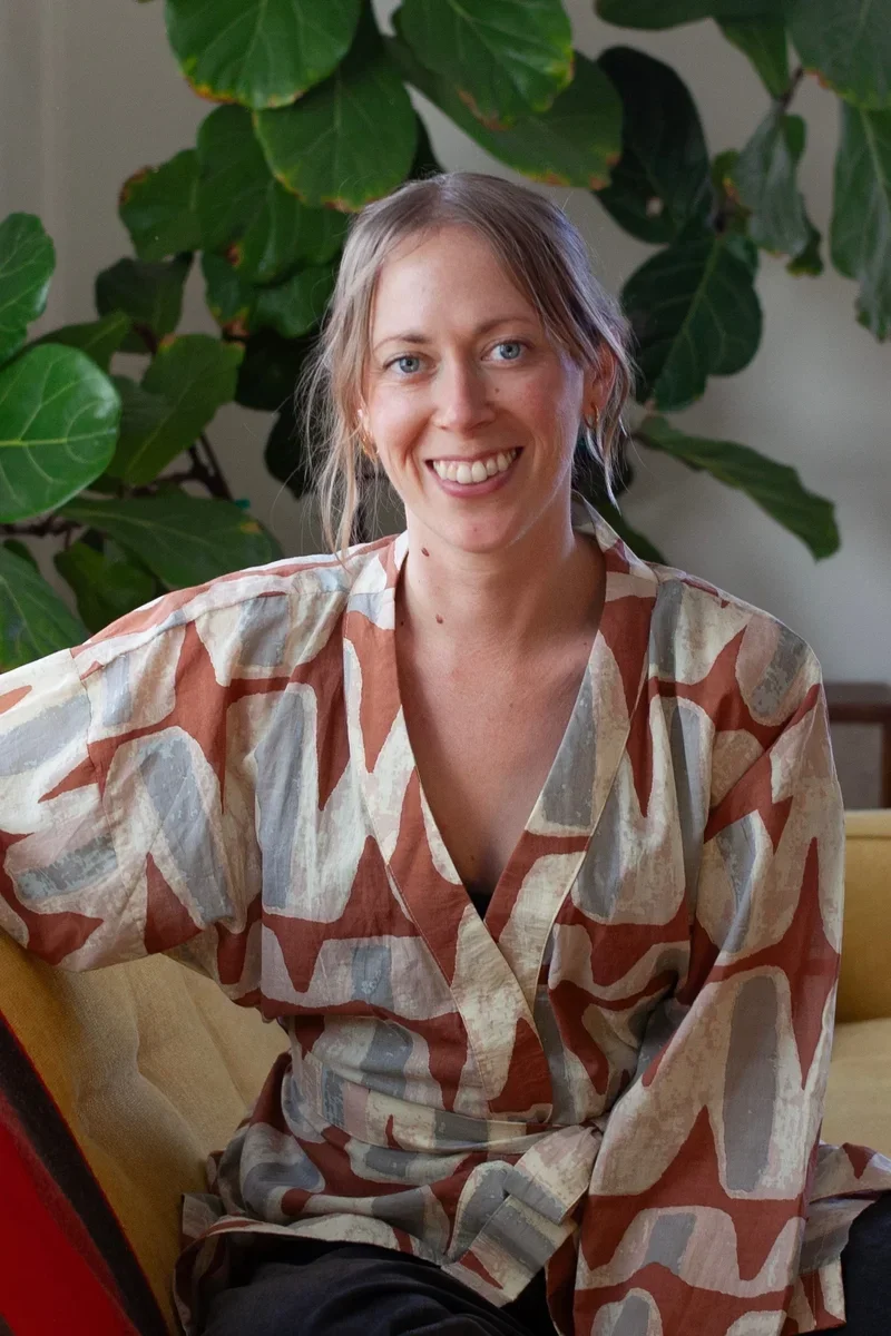 Dana Kurth, AMFT, smiling on couch with green indoor fig tree in the background