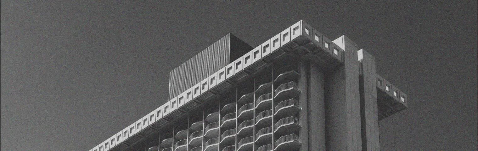 Close-up of the upper floors of a modern glass building at night, illuminated against a dark sky.