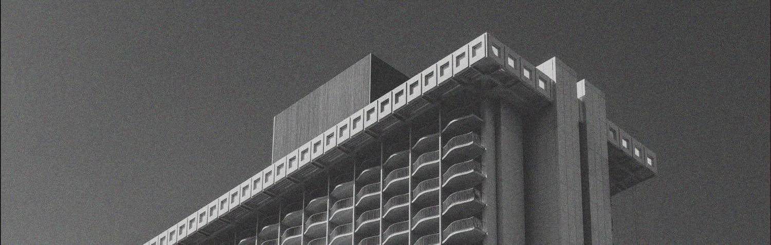 Close-up of the upper floors of a modern glass building at night, illuminated against a dark sky.