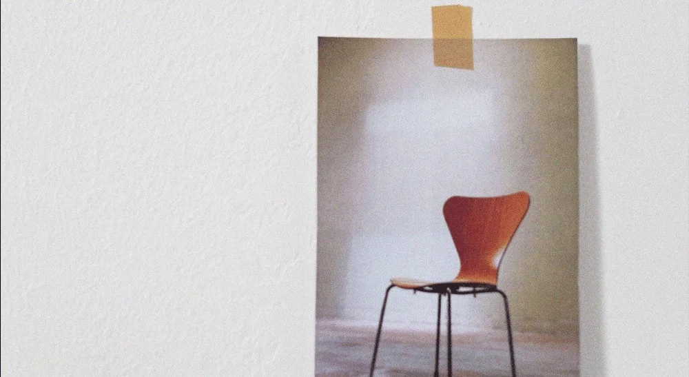 Empty wooden chair with black metal legs in a small nook with white walls.
