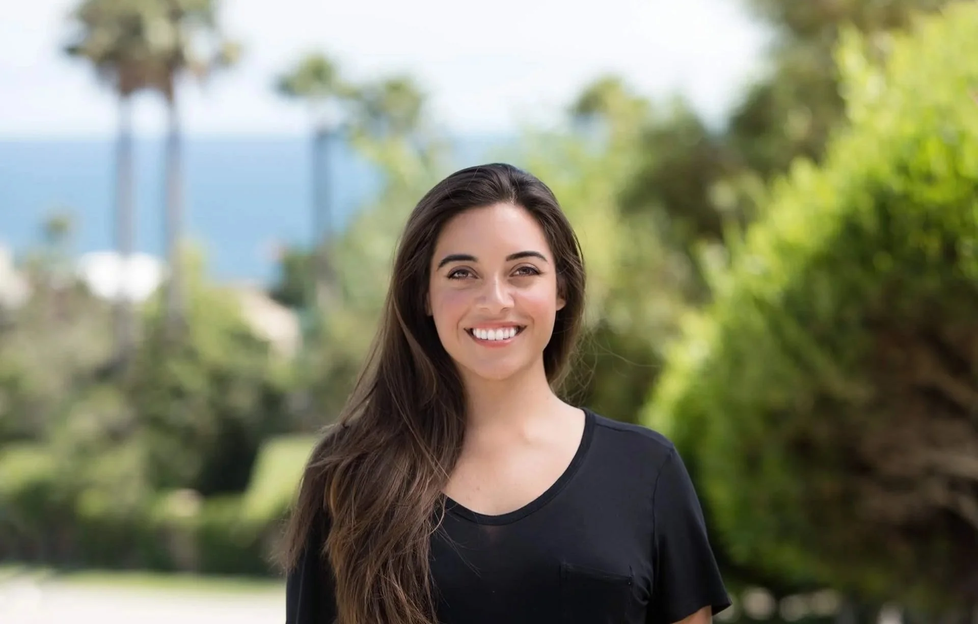 Dr. Sylvia Martin wearing a black top outdoors with green trees and a blue sky in the background.