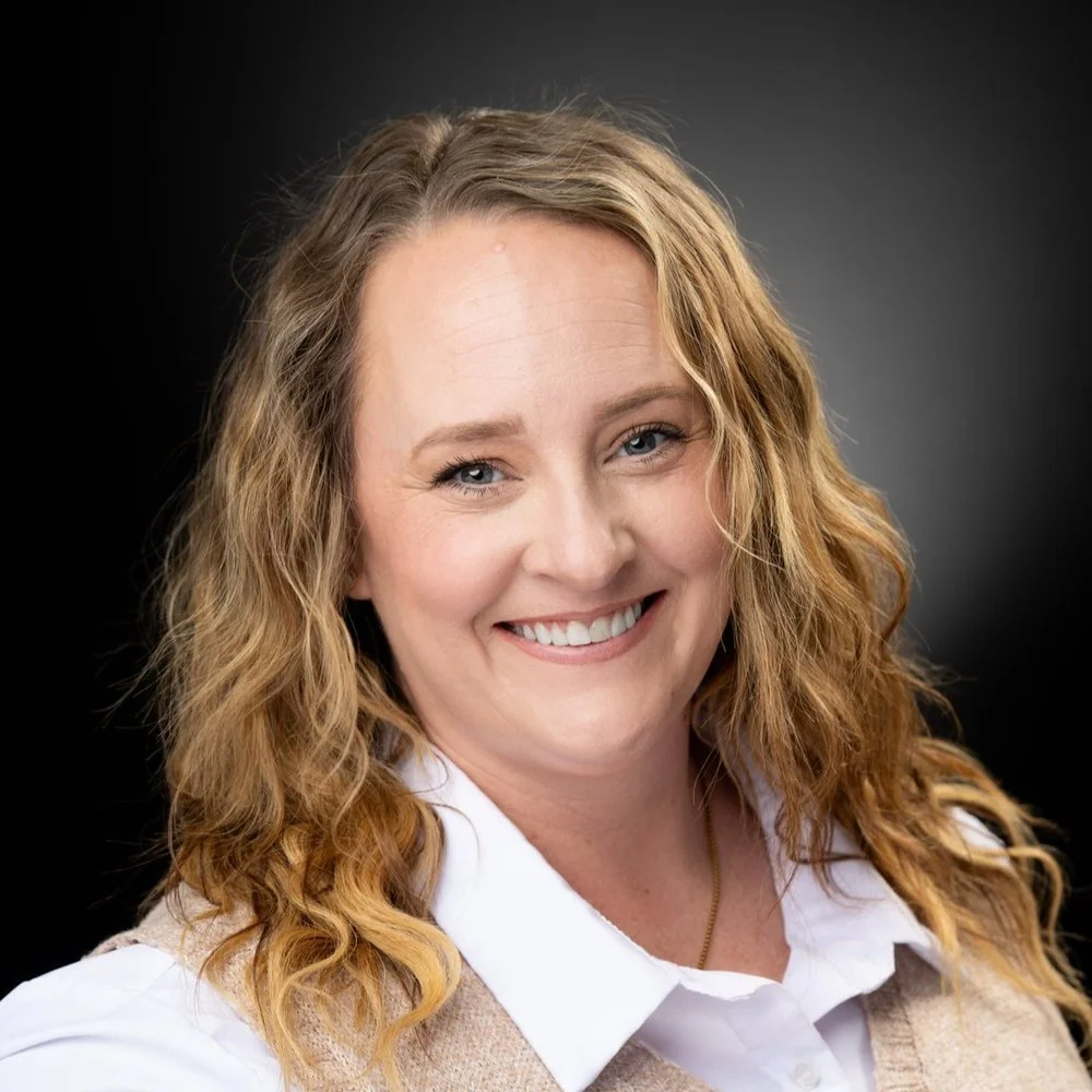 A woman with long curly red hair smiling against a dark background.