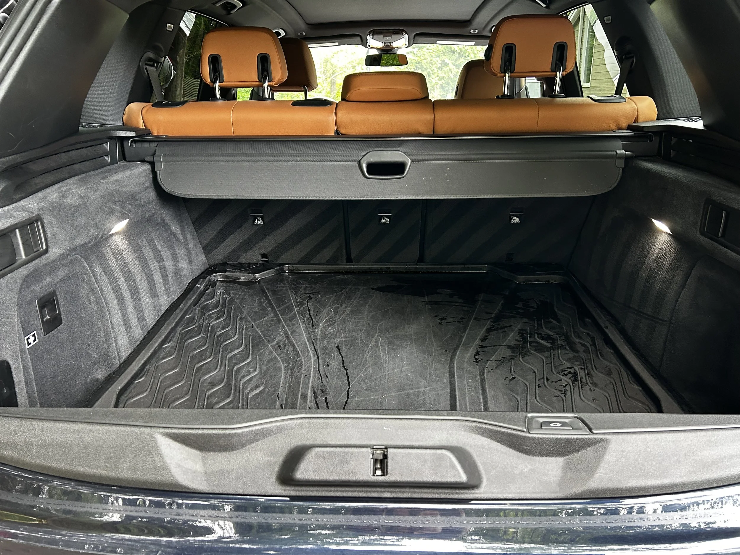Intérieur du coffre d'un SUV avec sièges arrière en cuir marron et une surface de chargement en caoutchouc noir, éclairée par deux petites lumières.