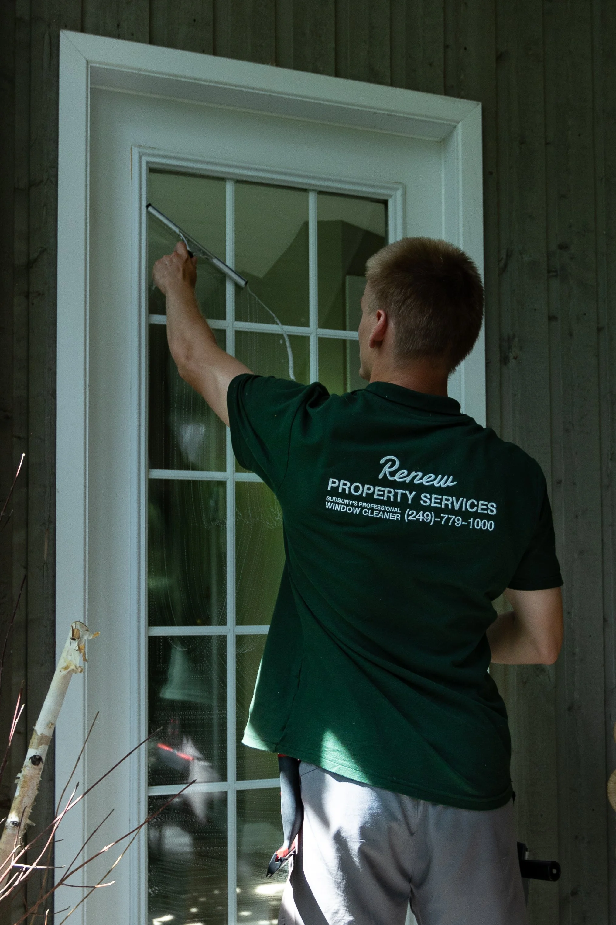Renew Property Services, 5 star rated window cleaner,cleaning a window in Sudbury ON with a squeegee. Renew uses both water-fed and tradition methods to clean windows