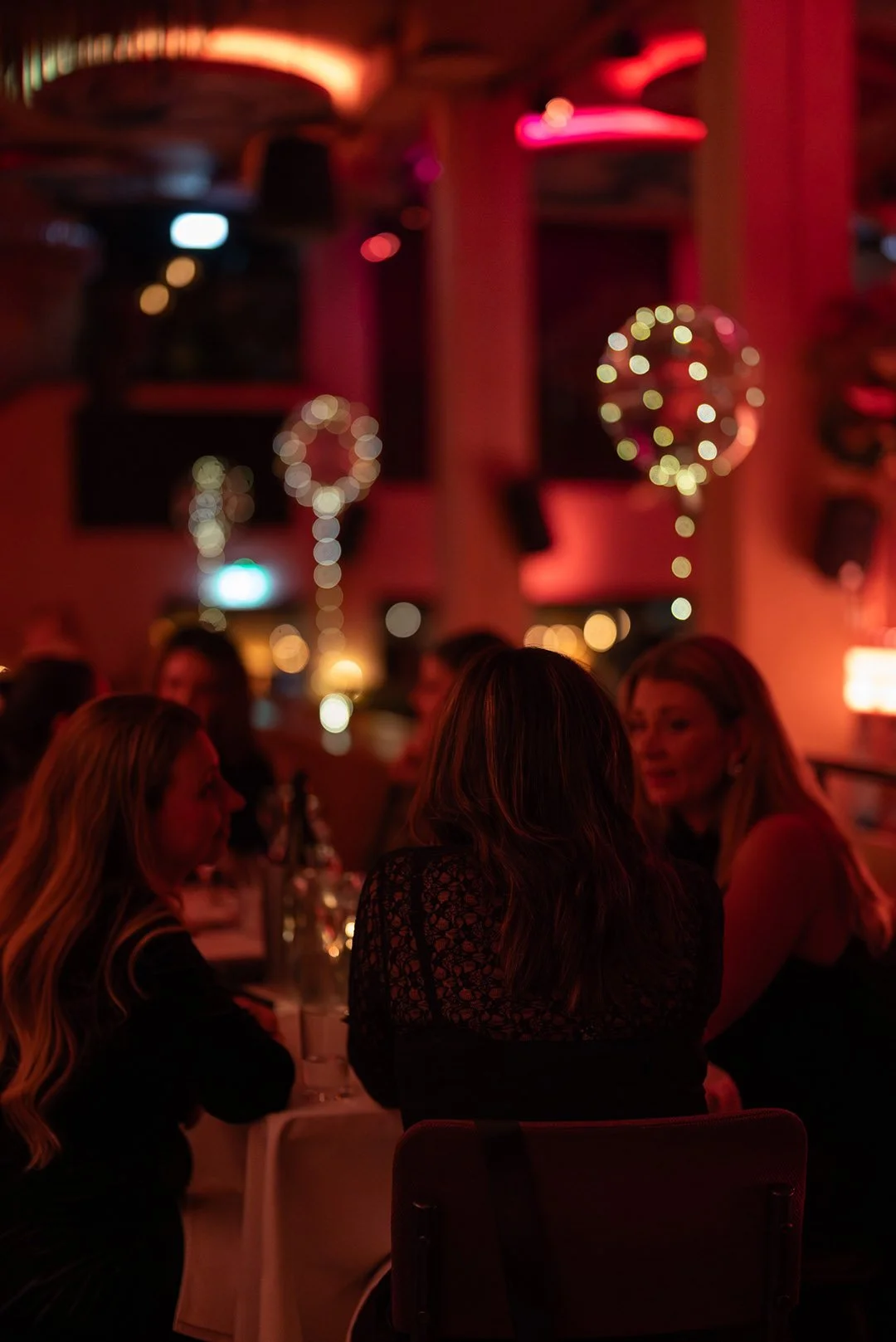 Flera kvinnor sitter vid ett bord i en restaurang med dimrad belysning och juldekorationer, inklusive julgranskulor.