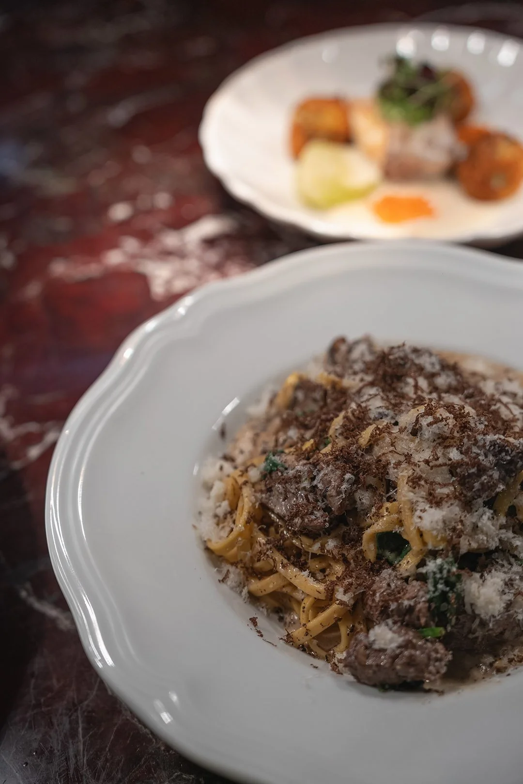 En tallrik med pasta med kött och grönsaker samt riven ost, och en annan assiett i bakgrunden med olika små rätter och lime.