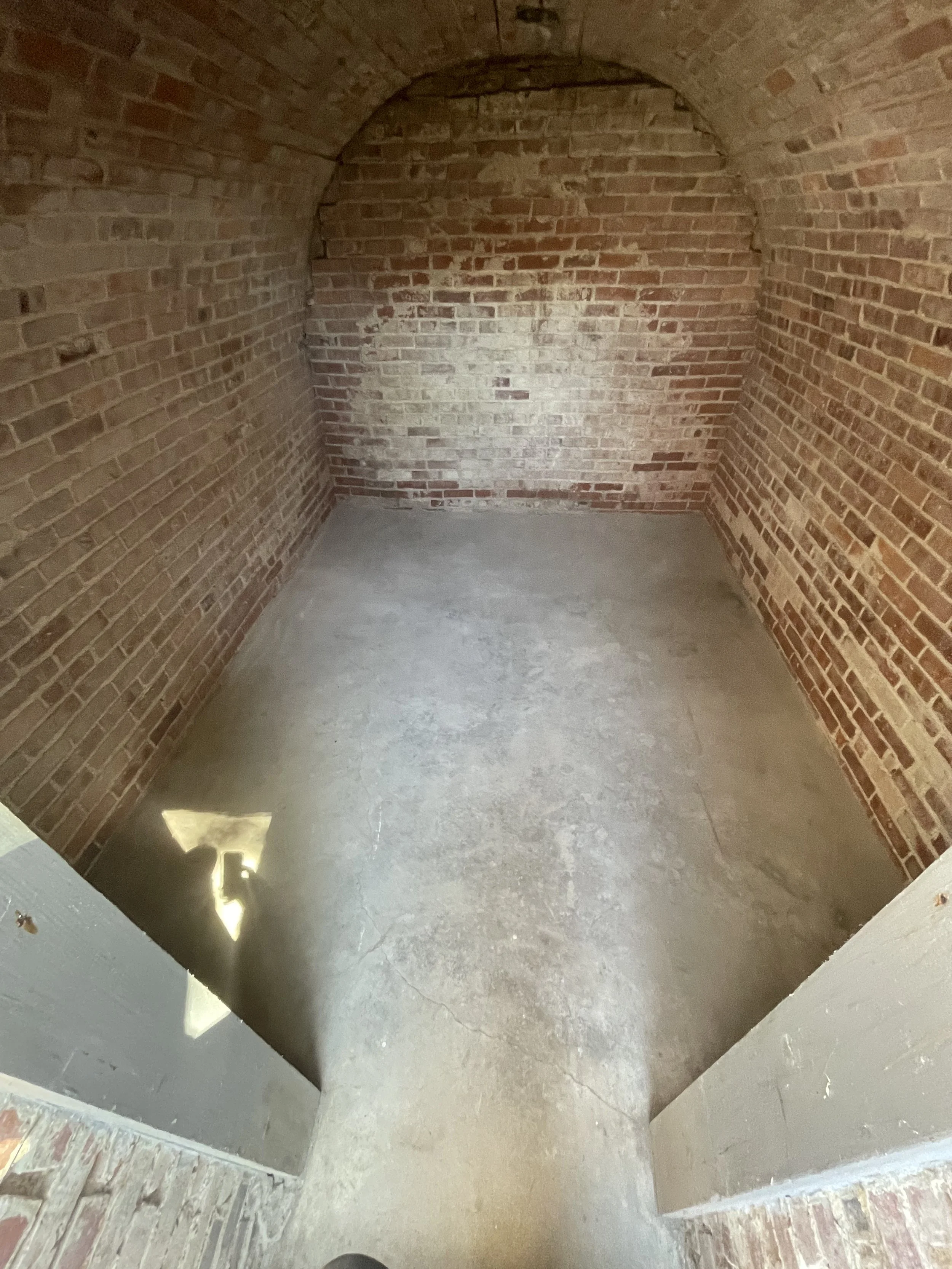 Empty brick room with arched ceiling and concrete floor, seen from doorway.