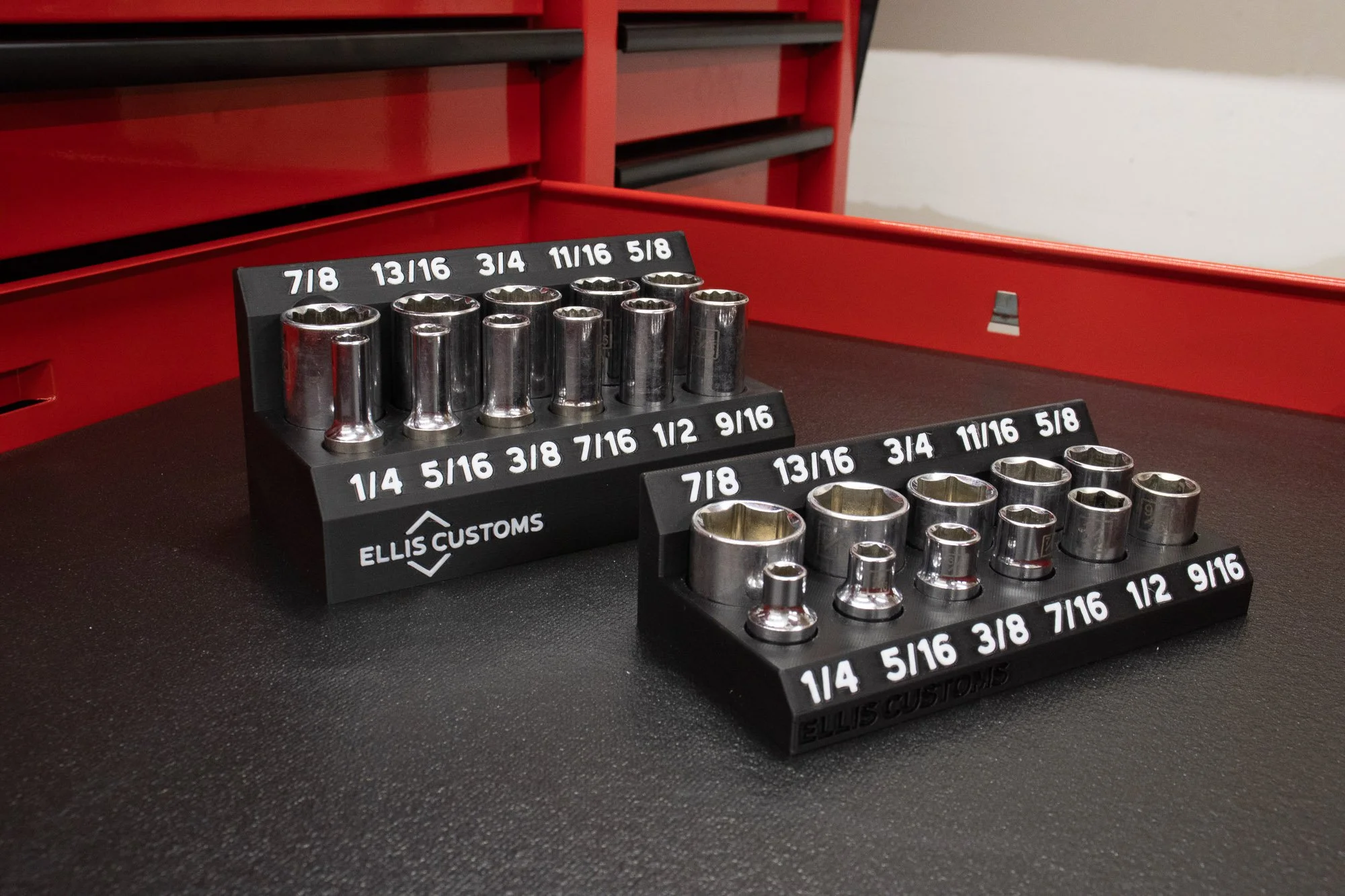 Set of chrome sockets and deep sockets arranged in black socket organizer inside tool box drawer with size labels in white.