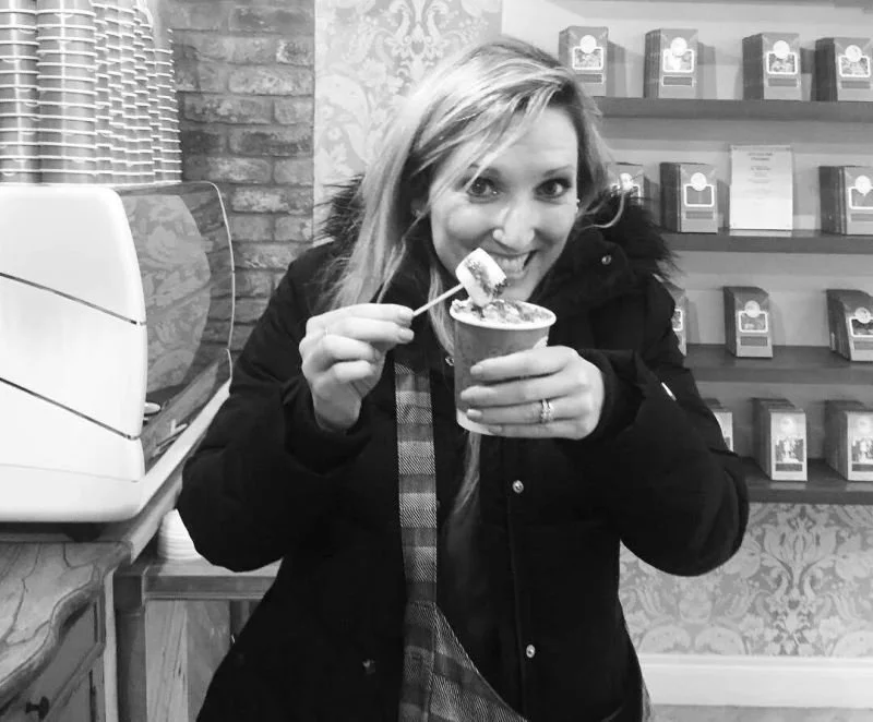 Jenny smiling while eating ice cream in a cup inside a shop with shelves of packaged products behind her.