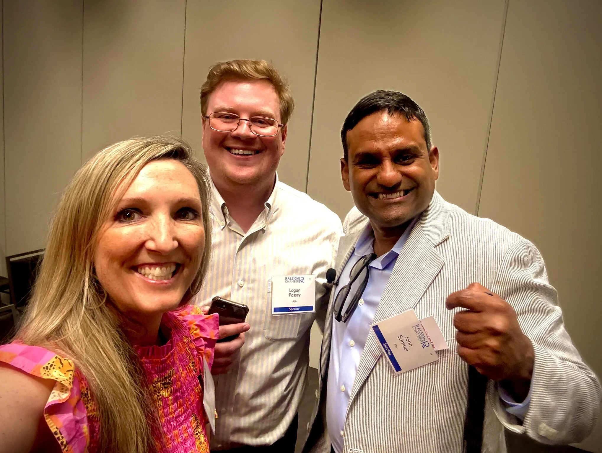 Three smiling people at a conference, two men and one woman, wearing name tags.