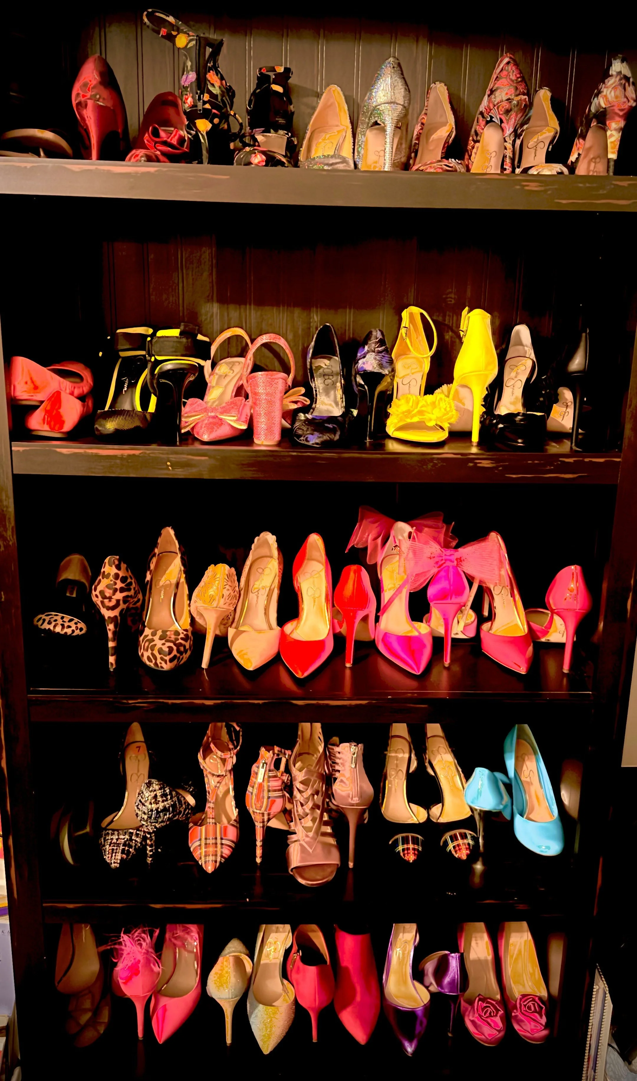 A display of colorful high-heeled shoes and boots arranged on black shelves in a store, including various styles and patterns.