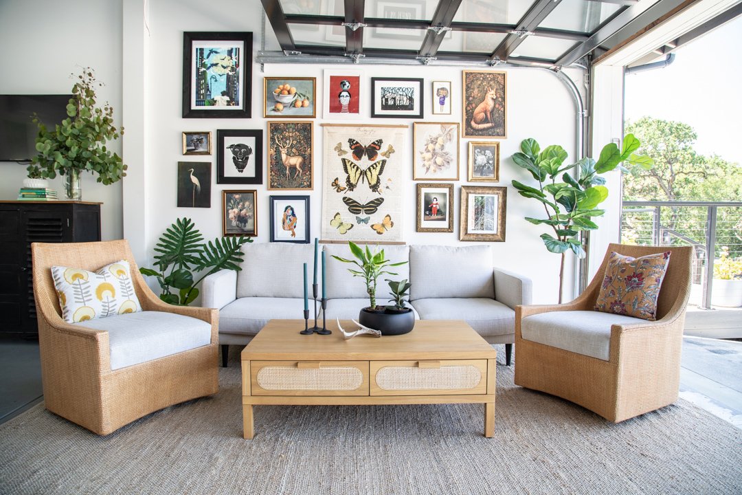 Living room with white sofa, two rattan armchairs, wooden coffee table, and gallery wall with framed artwork and butterflies.