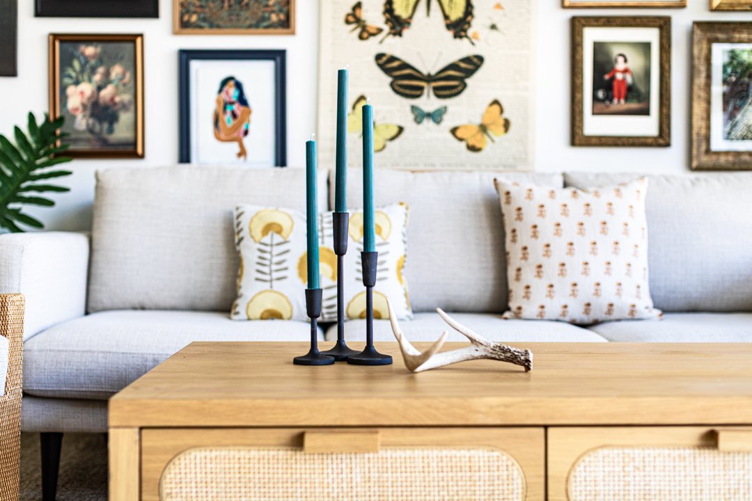 Living room with a white couch, decorative pillows, artwork and butterfly wall art, and a wooden coffee table with teal and black candles and an antler decor piece.