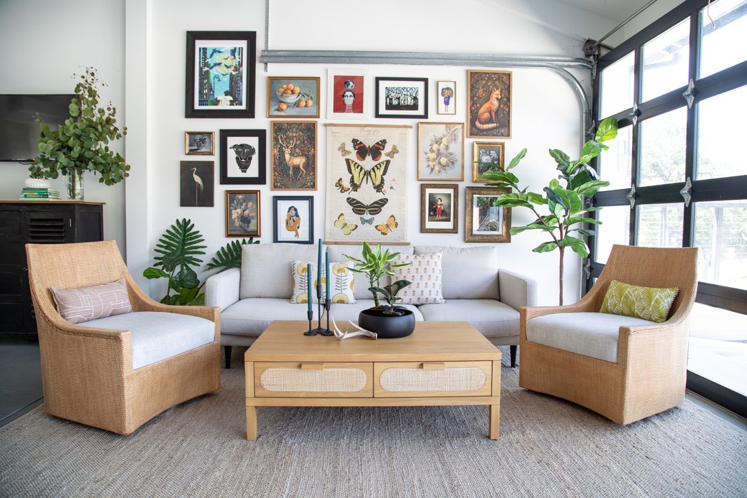 Living room with a gray sofa, two beige armchairs, a wooden coffee table, houseplants, and a gallery wall with framed artwork and photographs.