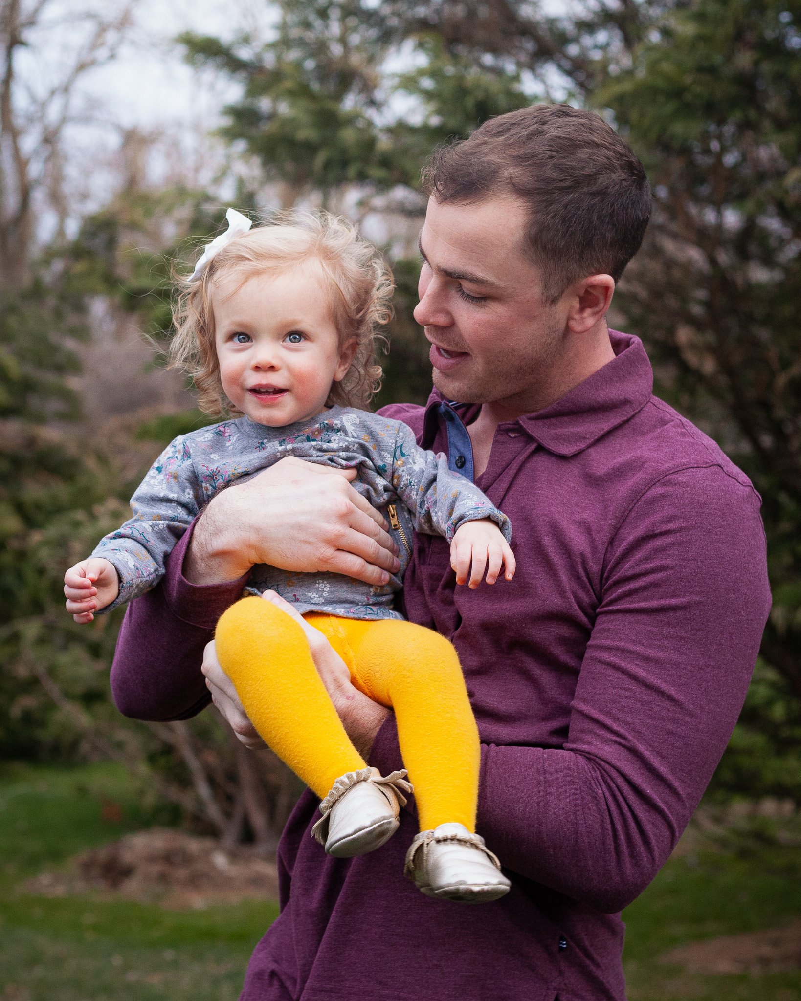 A man holding a smiling young girl outdoors in a park with trees in the background.