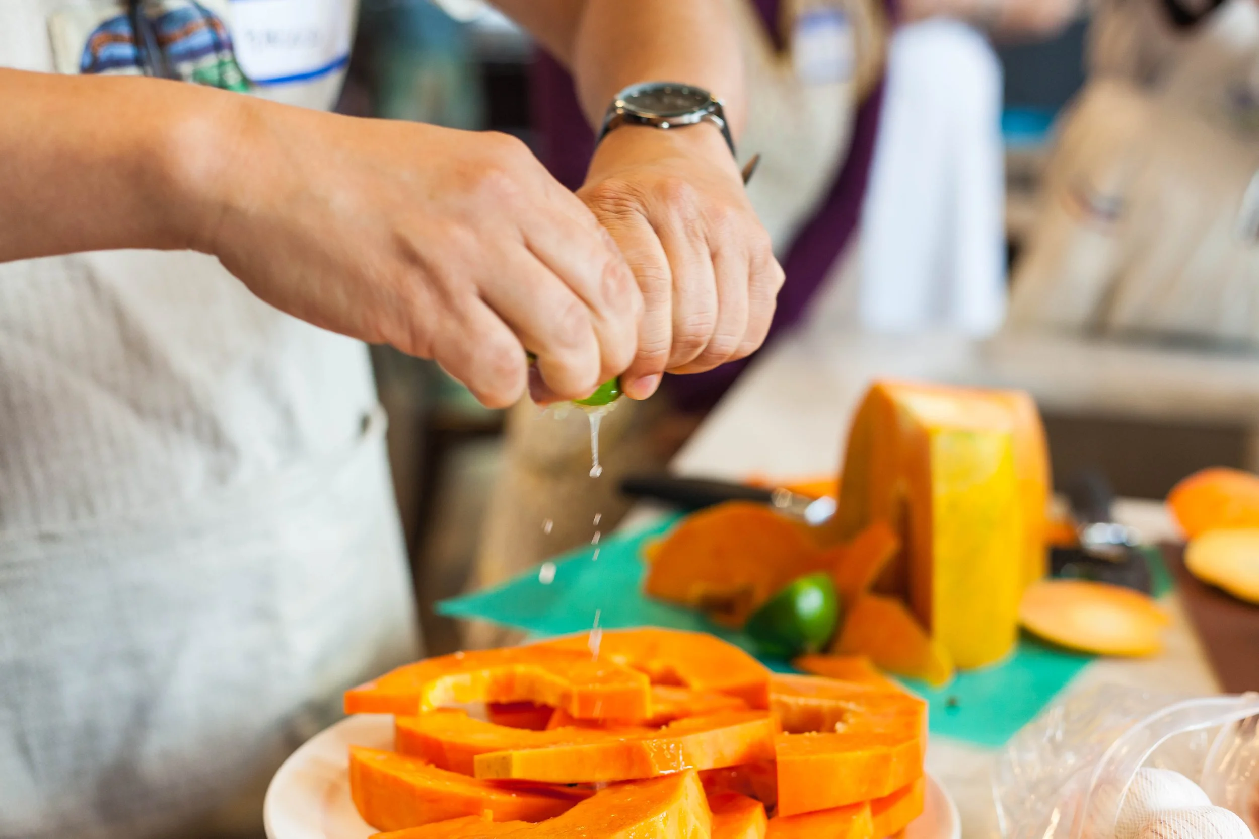 Documentary event photography of a person squeezing a lime over chopped papaya on a white plate in a kitchen at a community event in Richmond, VA. 