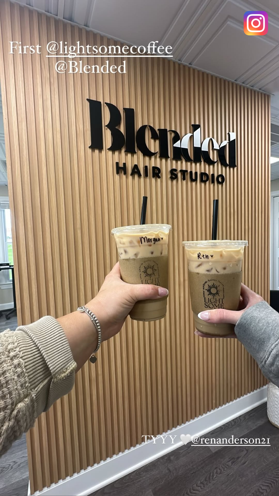 Two iced coffee drinks with personalized labels, held up in front of a wooden wall with a black sign that reads "Blended Hair Studio."