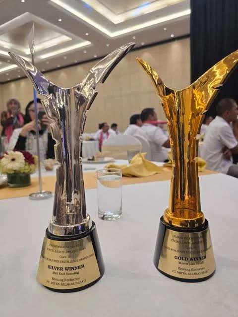 Silver and gold trophies on a table with people in the background at an event.