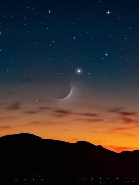 Night sky with stars and a crescent moon over a silhouette of mountains at sunset.