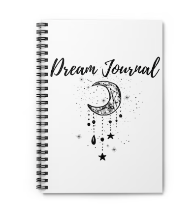 A white spiral-bound notebook titled 'Dream Journal' with a black and white illustration of a crescent moon, stars, and a hanging crystal