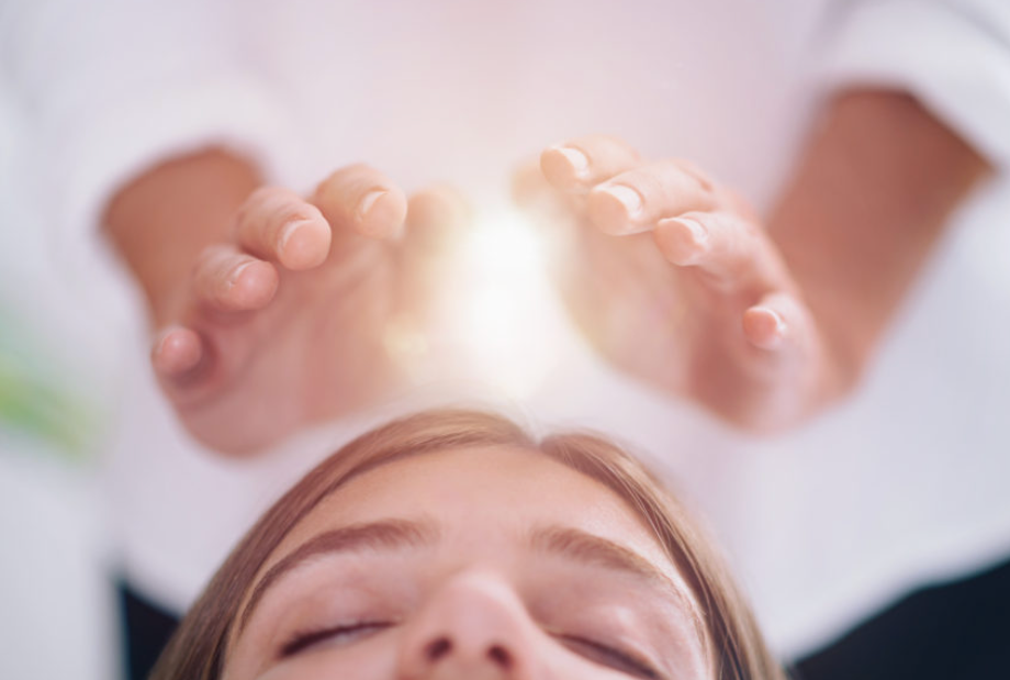 A person receiving Reiki healing treatment with hands positioned above their forehead.