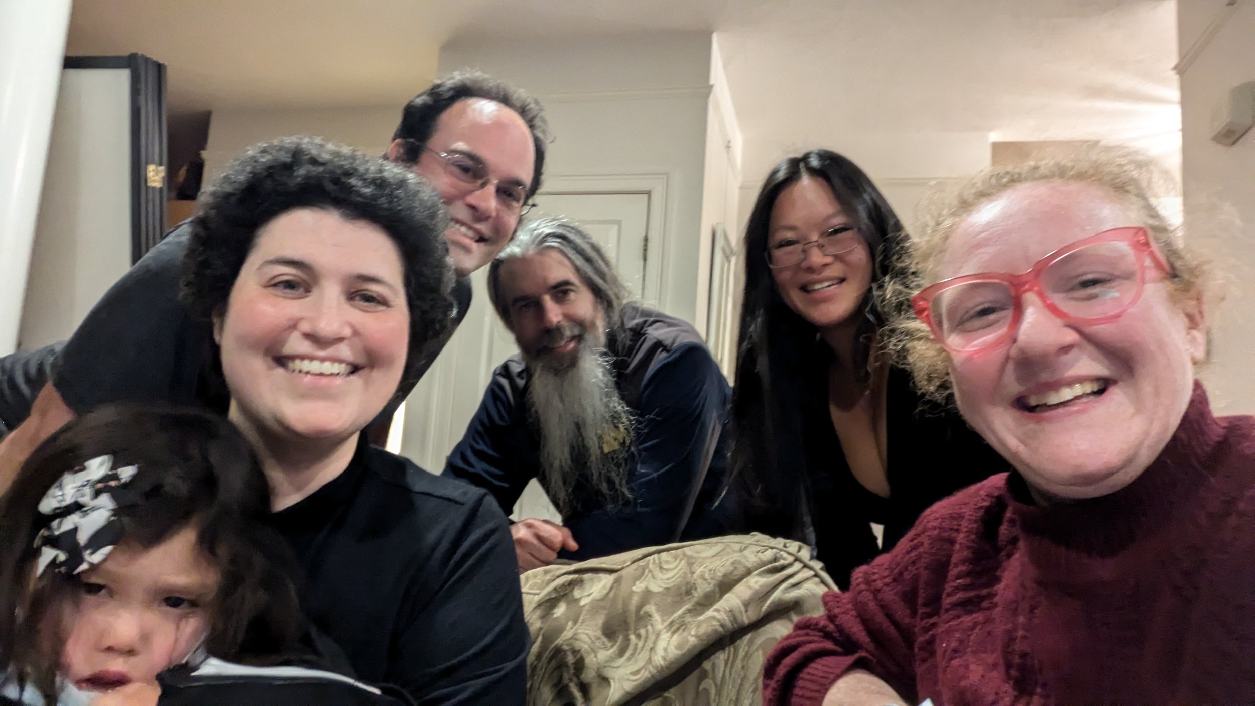 Group of six people smiling at a gathering, some standing and some sitting, indoors.