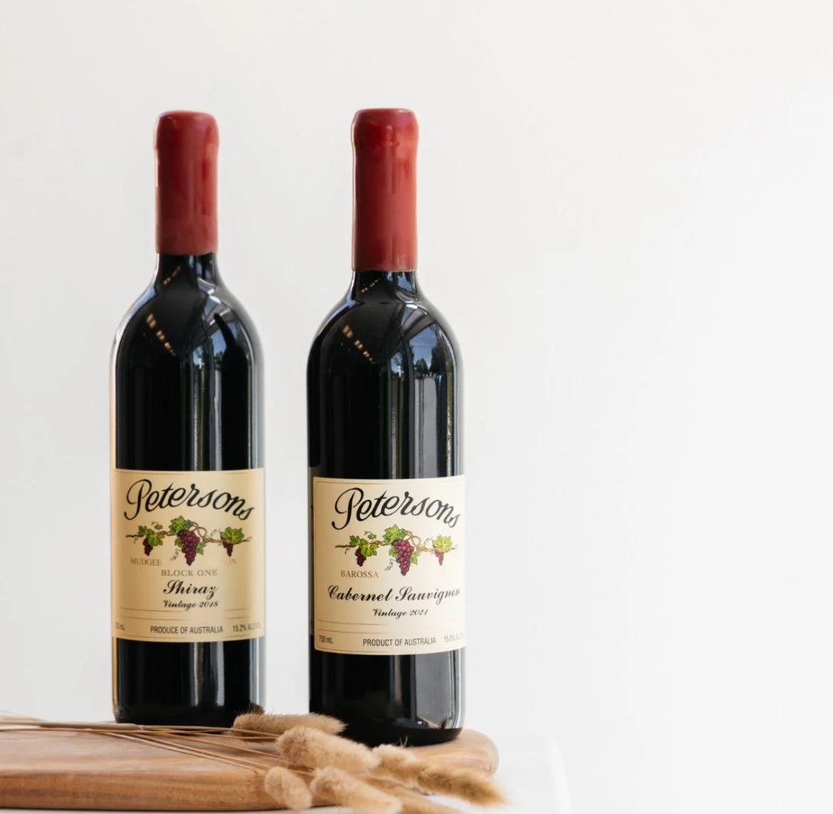 Two bottles of Peterson wine, one Shiraz and one Cabernet Sauvignon, on a wooden surface against a plain white background.