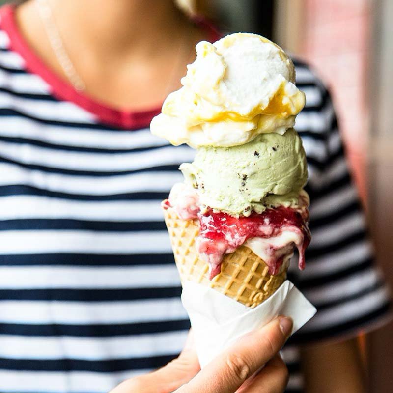 Person holding a three-scoop ice cream cone with vanilla, green, and strawberry flavors.