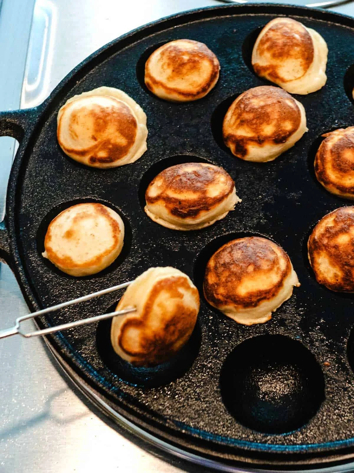 Cooking takoyaki balls on a cast iron pan, with one being lifted with a skewer.