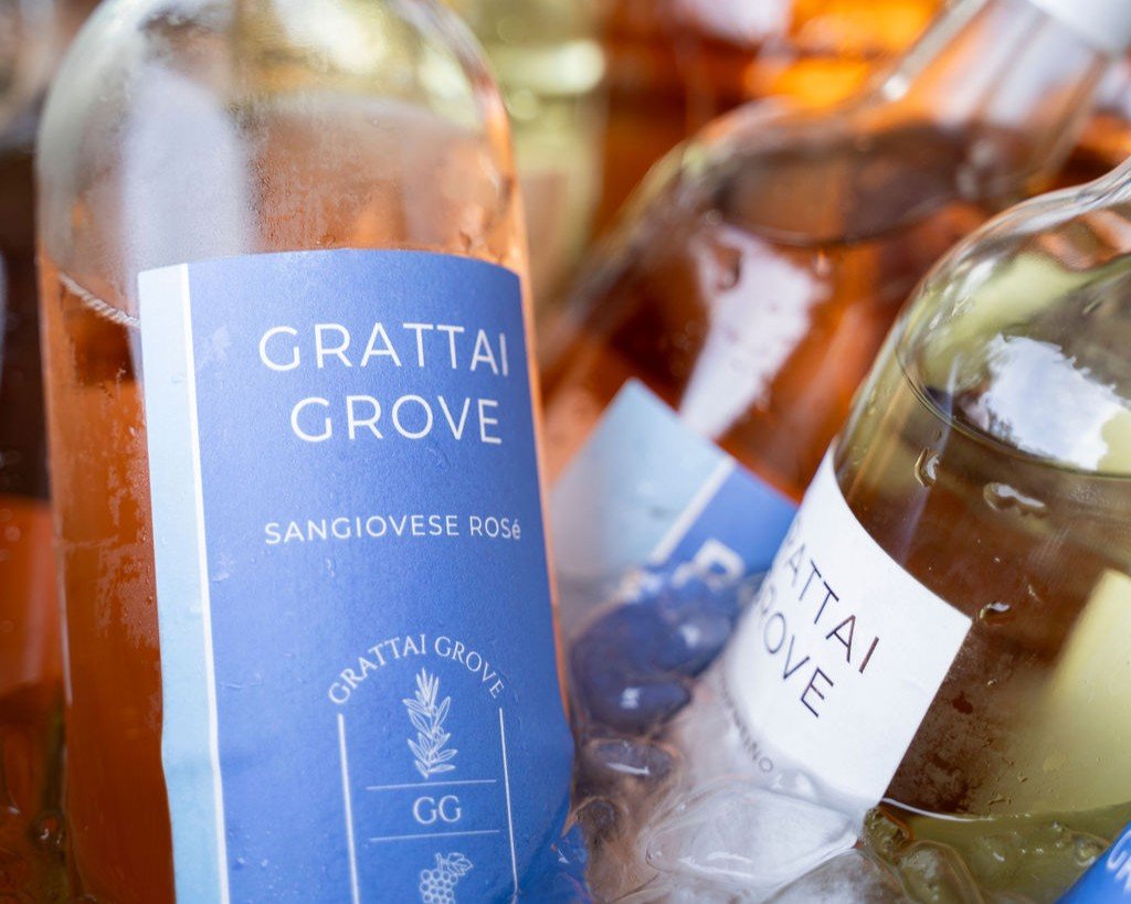 Six bottles of wine, three rosé and three cabernet sauvignon, arranged on a mosaic table outdoors with trees in the background.