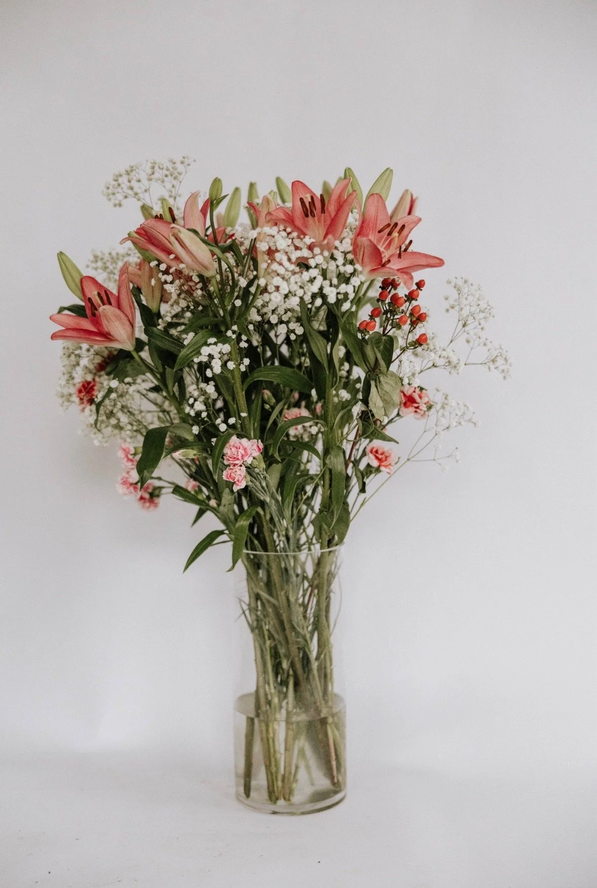 Bouquet of pink lilies, baby's breath, and greenery in a clear glass vase.