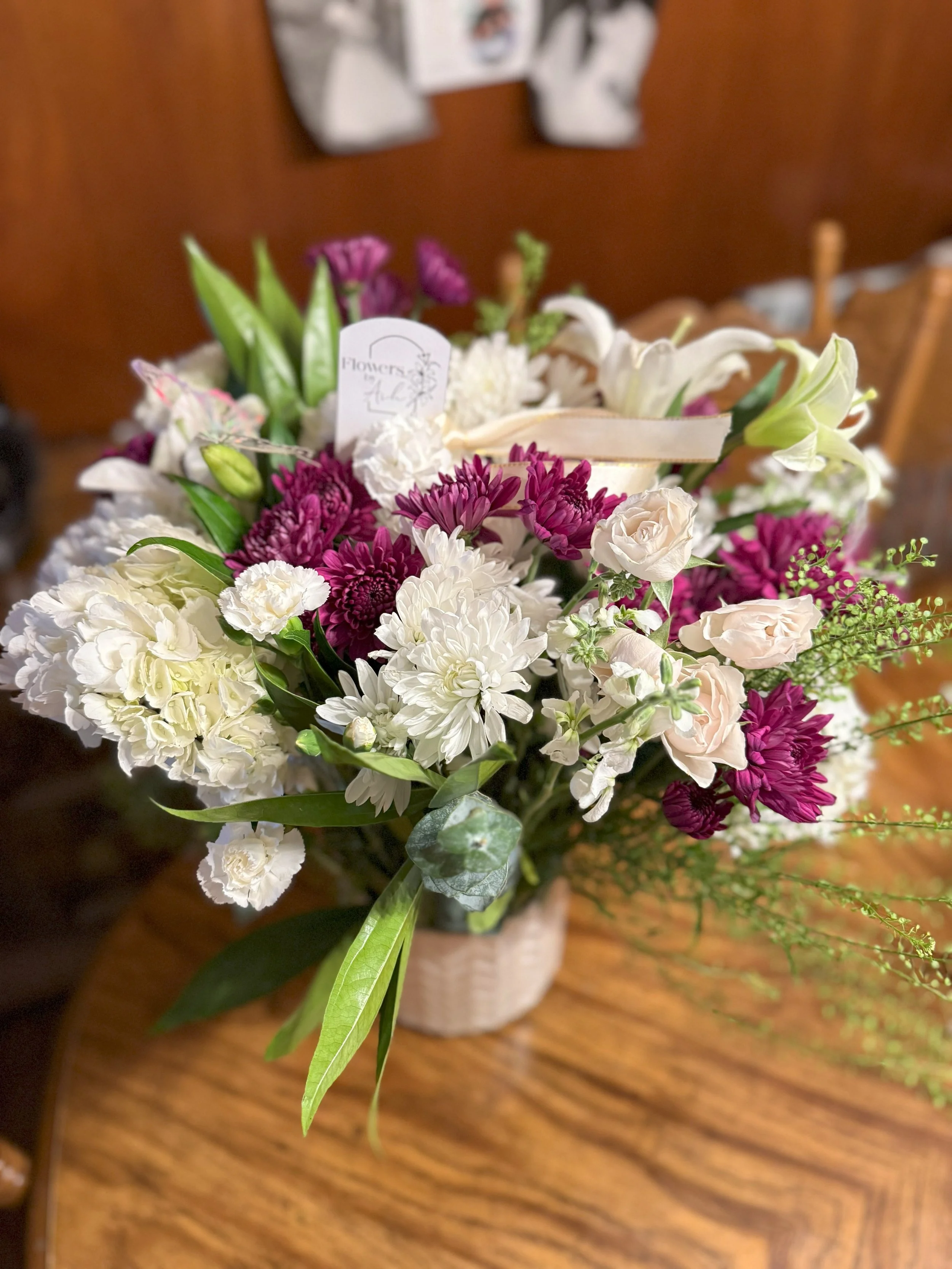 Flower arrangement with white and purple flowers in a vase on a wooden table.