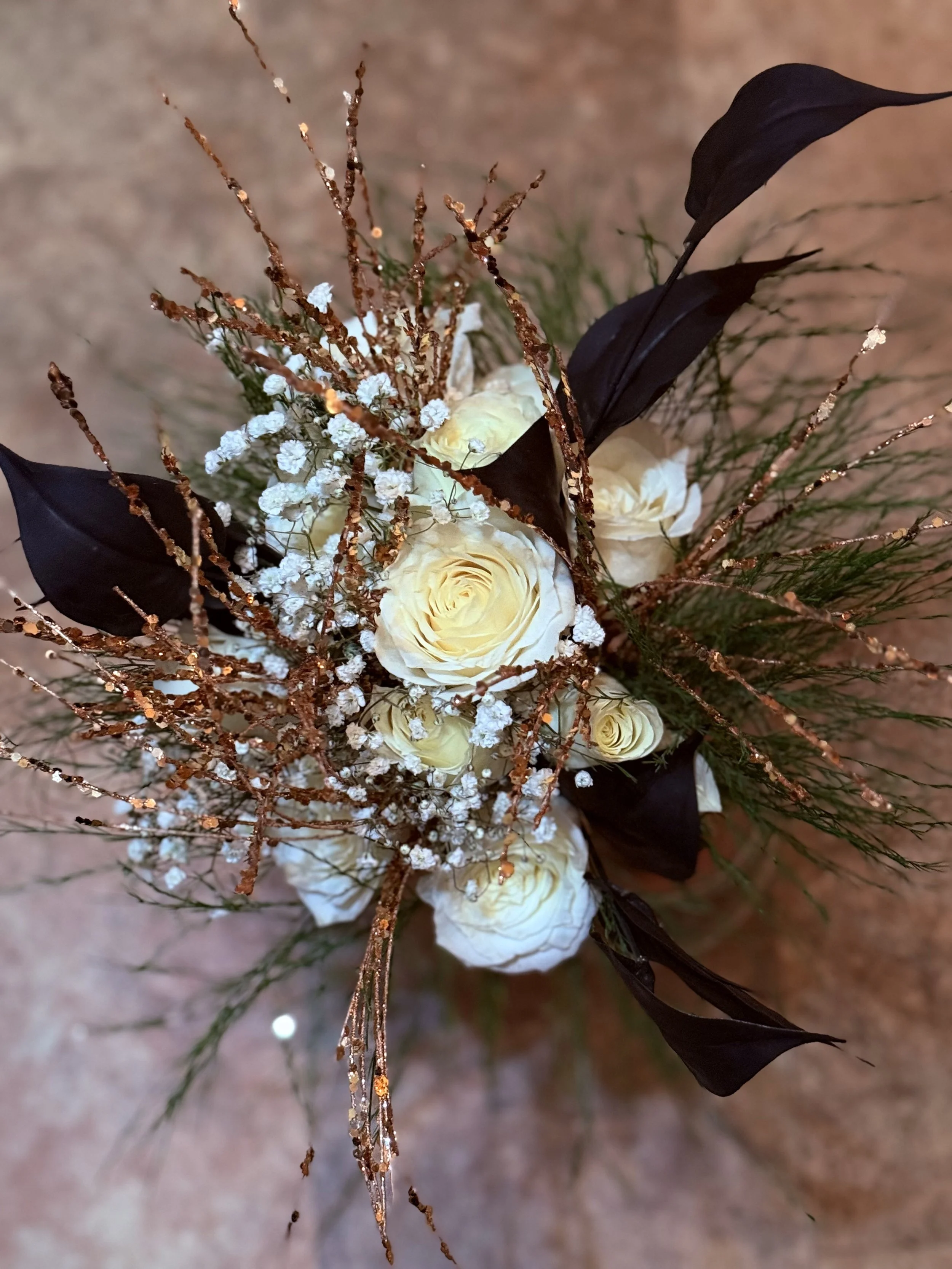 Bouquet of white roses with dark calla lilies, baby's breath, decorative branches, and greenery.