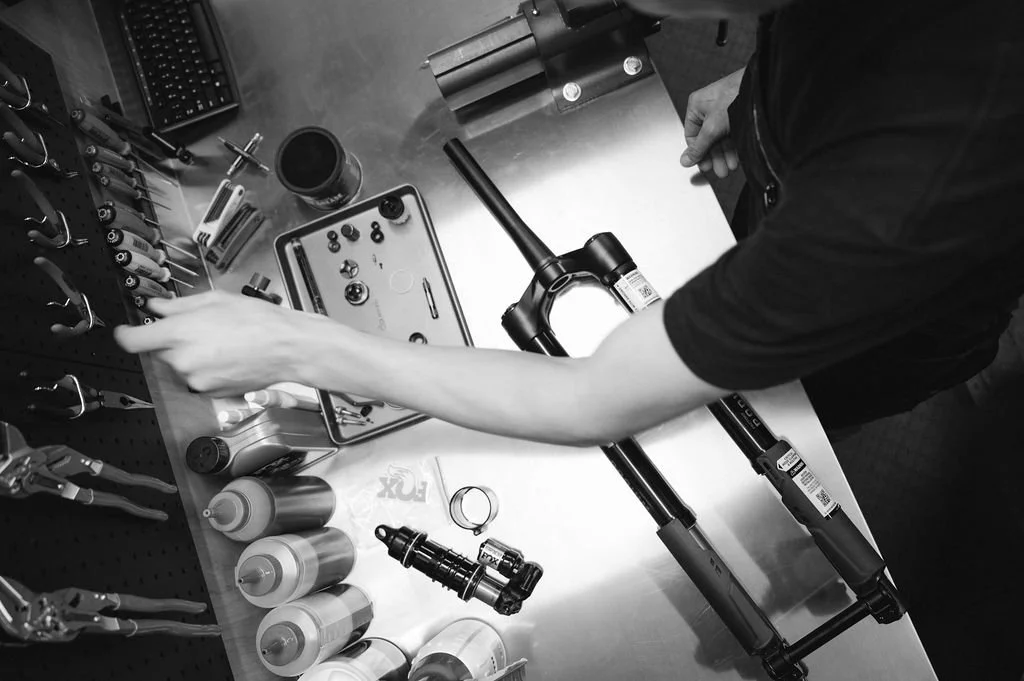 A person organizing bicycle components and tools at a workspace, including a bicycle fork, bolts, and various hand tools.